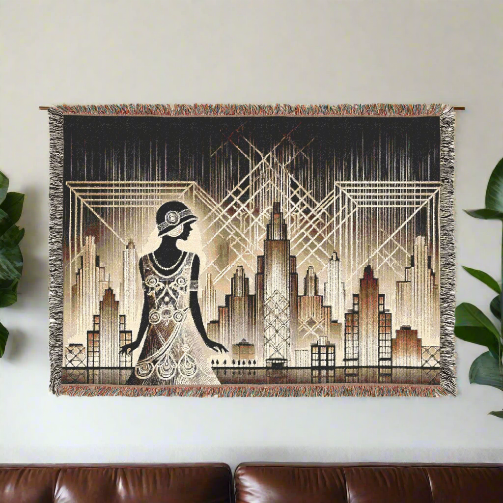 Art Deco woven blanket with a vintage flapper design and a city skyline in gold and cream, framed by geometric patterns, displayed on a wall above a leather couch with green plants on either side.