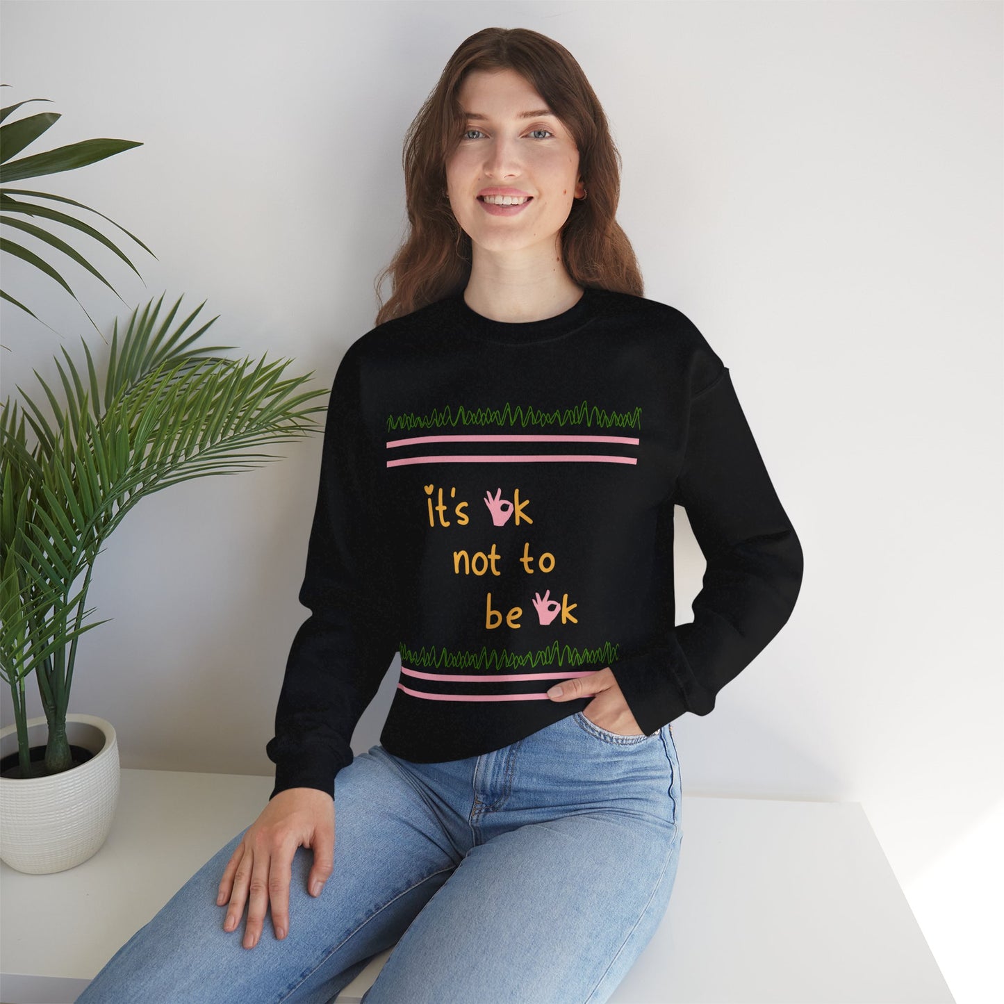 Lifestyle image of a woman wearing the 'It’s OK Not To Be OK' crewneck sweatshirt in black, highlighting the front design