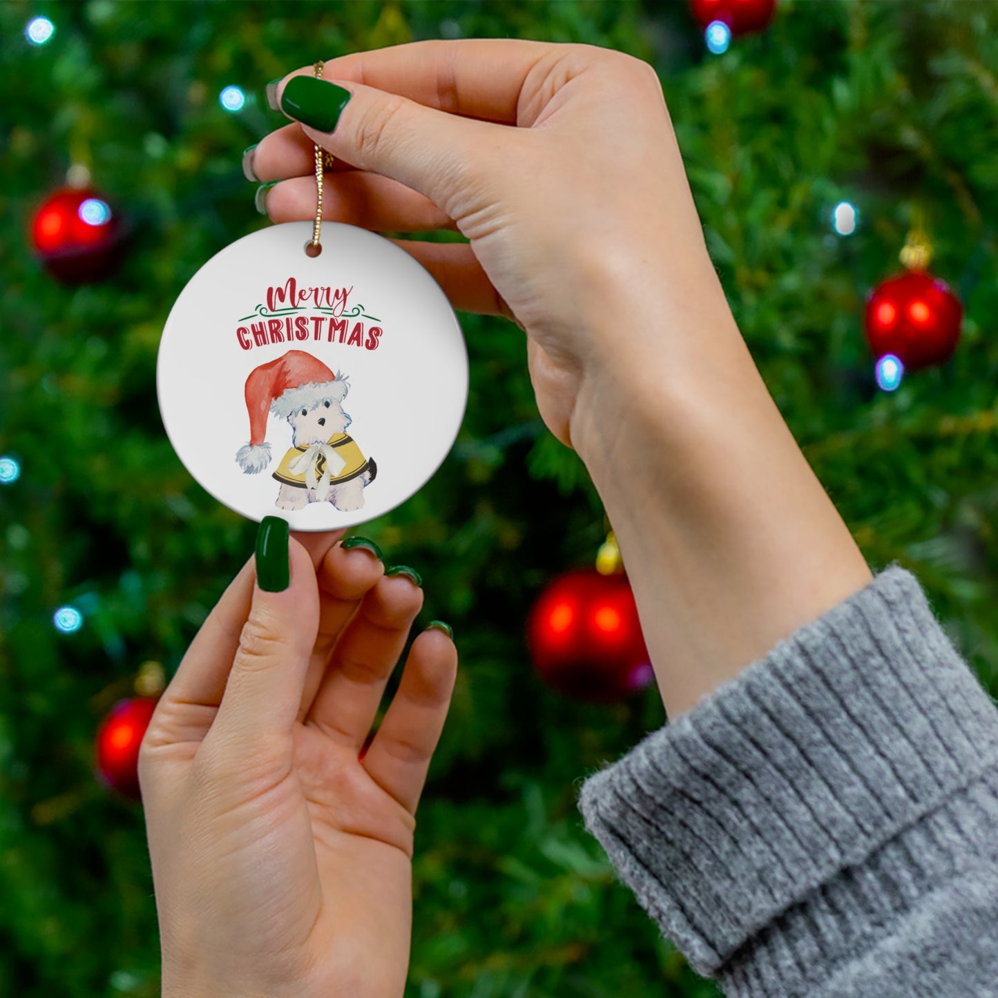 Bitsy the puppy Christmas ornament, ceramic with festive text and adorable holiday dog design, hung by a gold string against a festive Christmas Tree.
