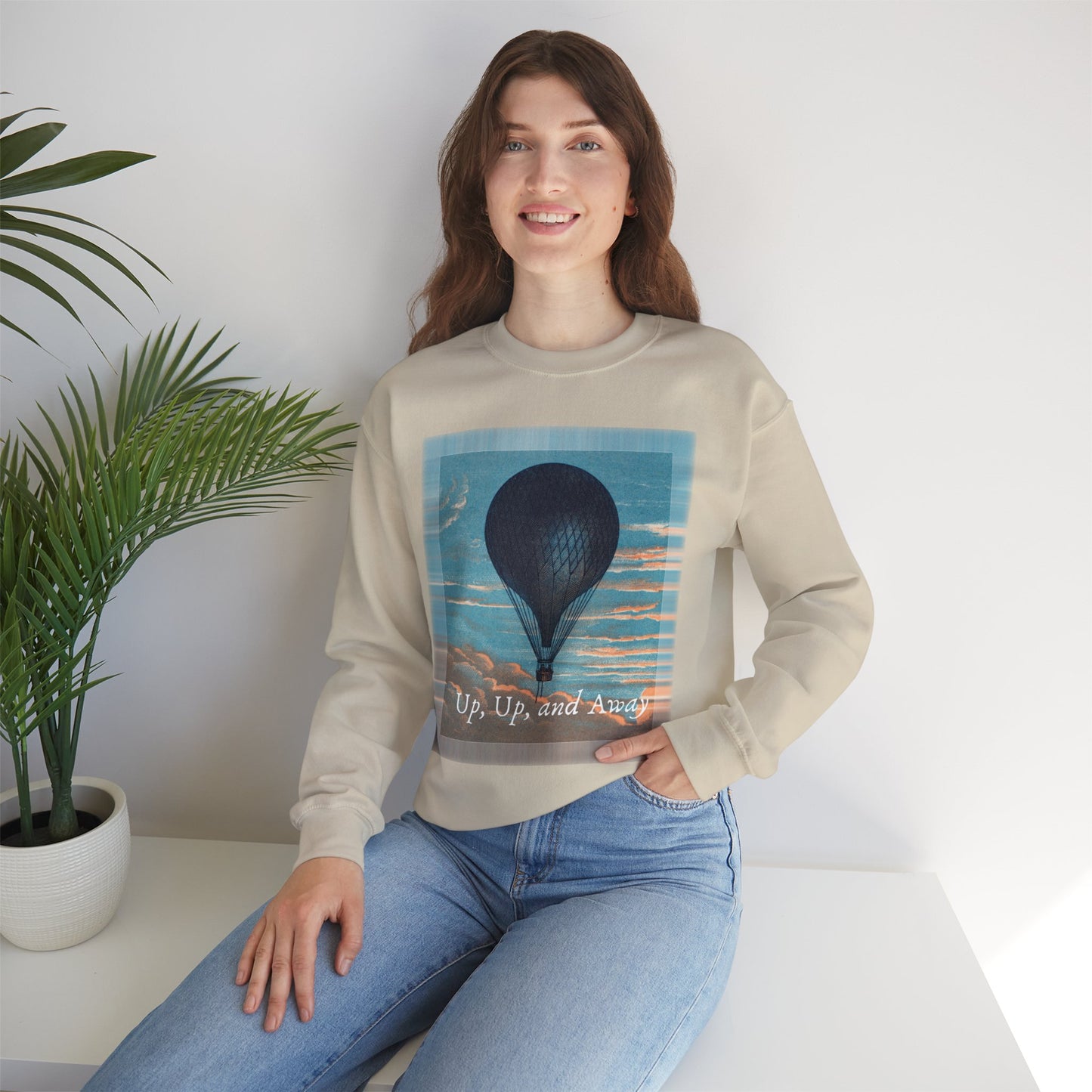 Lifestyle image of a woman wearing the "Up, Up, and Away" sweatshirt in sand, seated indoors