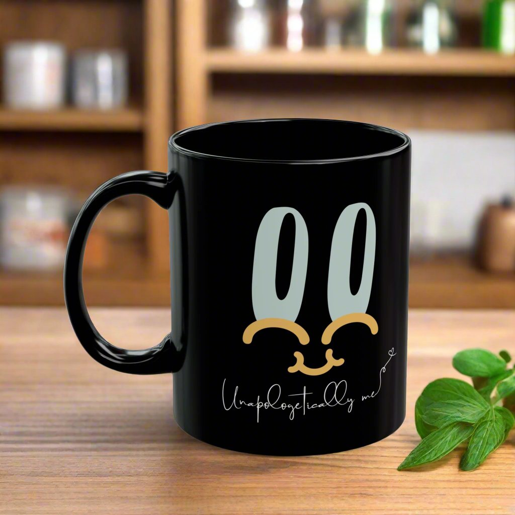 Lifestyle image of black mug on a counter featuring a playful smiley face design and "Unapologetically Me" quote in cursive.