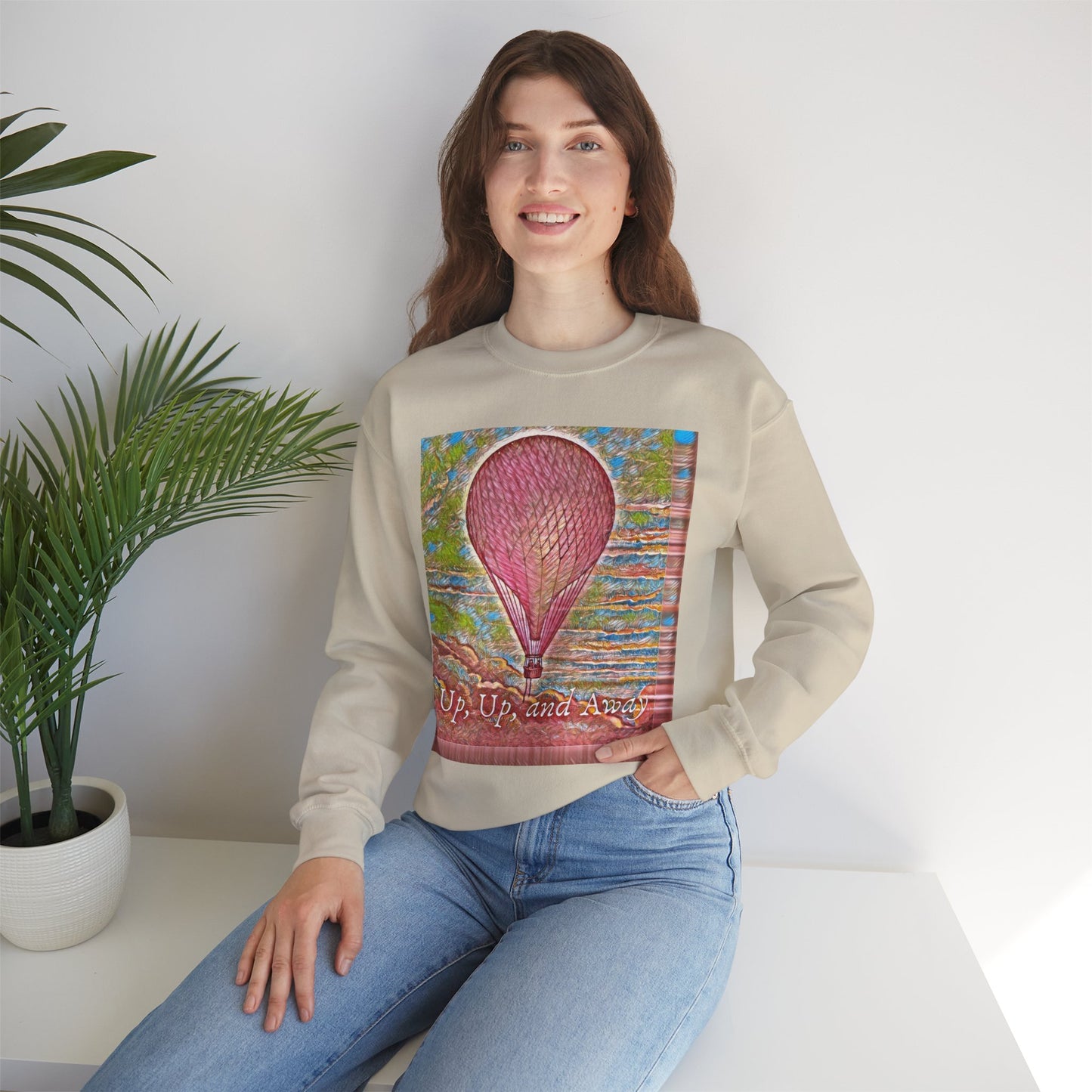 Lifestyle image of a woman wearing the pink hot air balloon sweatshirt in sand, sitting indoors
