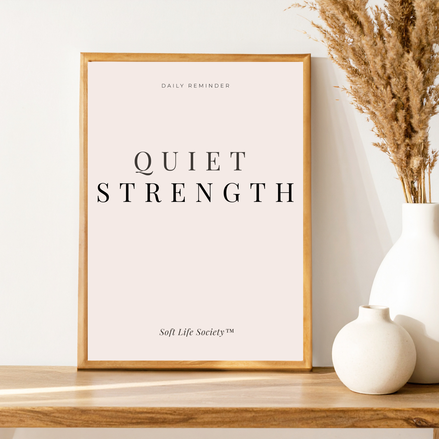 Framed print with 'Quiet Strength' text on a wooden surface with decorative vases.