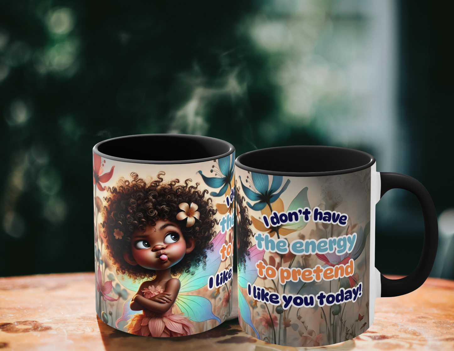 Two vibrant coffee mugs with a whimsical fairy design. The text on the mug reads "I don't have the energy to pretend I like you today!" with colorful floral patterns and an expressive fairy character. The mugs are placed outdoors on a wooden table, surrounded by a natural, green, blurry background.