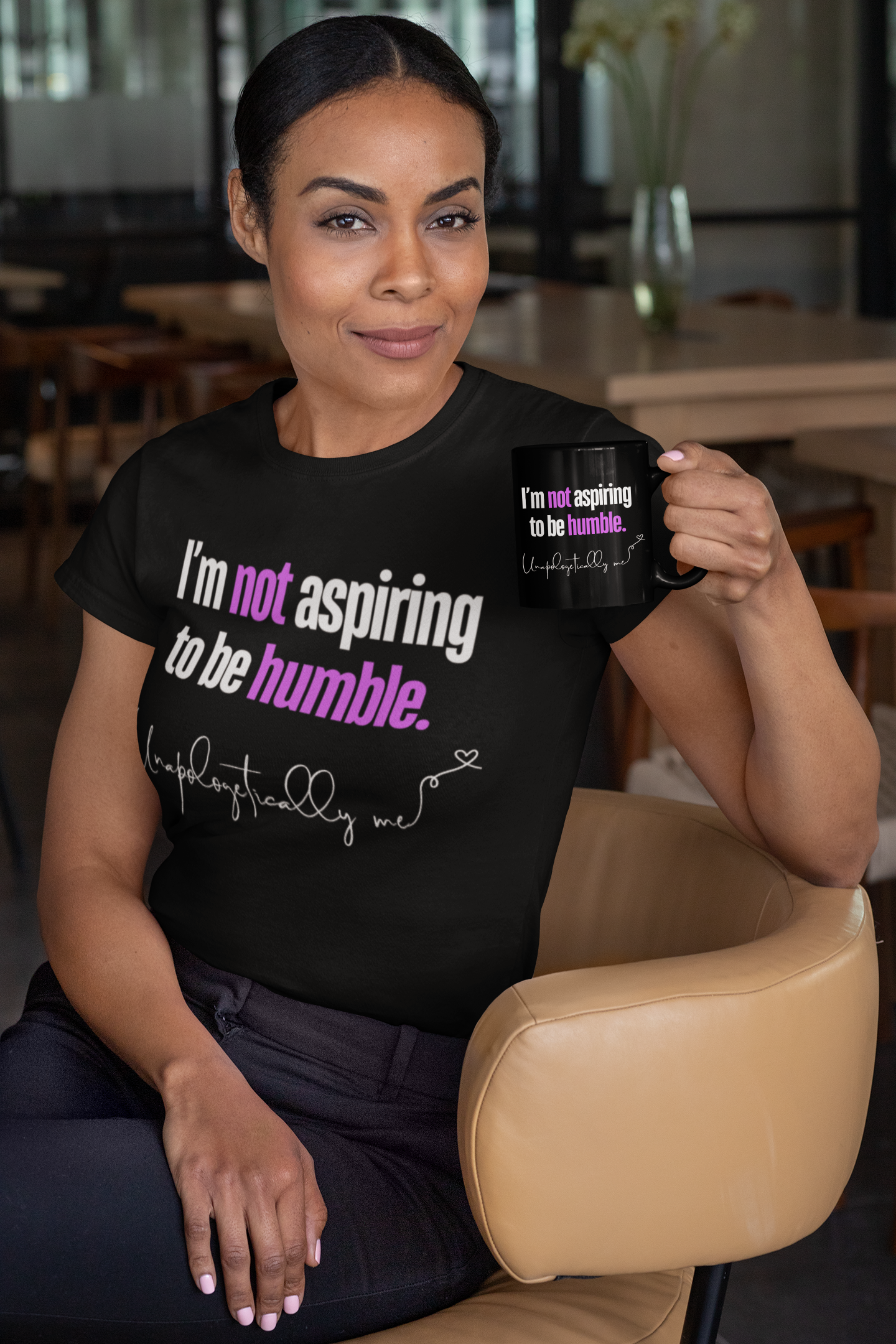 Lifestyle image of a model in a casual setting holding coffee mug and T-shirt featuring "I'm not aspiring to be humble." design