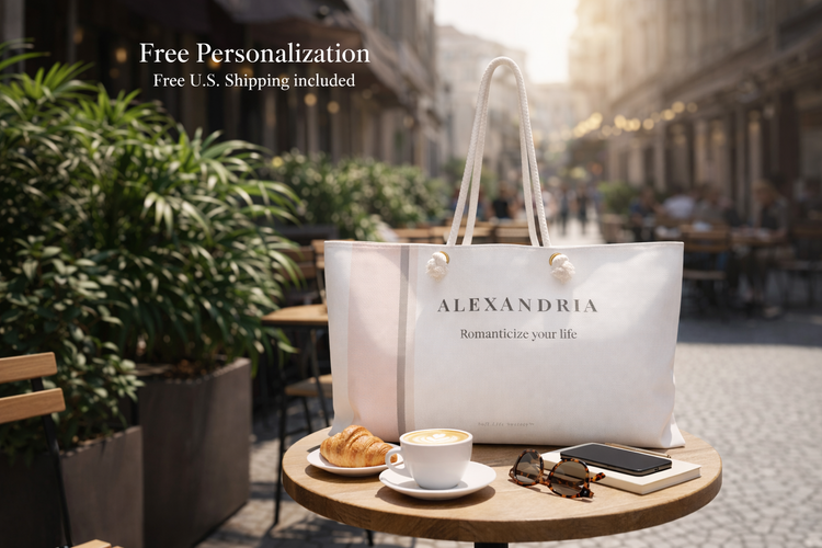 Personalized neutral weekender bag with name “Alexandria” styled on a café table with coffee and croissant, soft lifestyle travel aesthetic