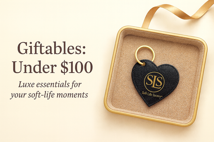 Black SLS heart-shaped Nappa leather keychain with gold monogram displayed on a beige suede jewelry tray with gold trim, styled with soft lighting for an elegant giftable look.