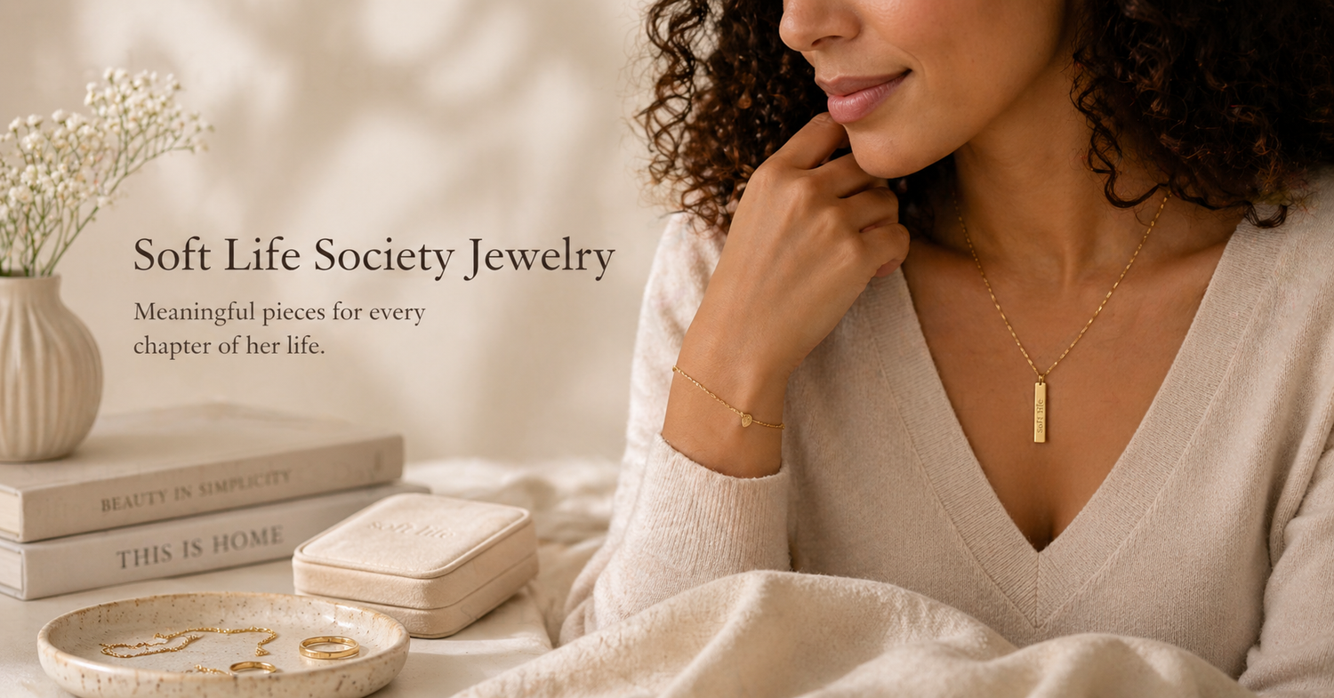 Soft Life Society jewelry collection banner featuring a woman wearing a gold bar necklace in a warm, neutral-toned lifestyle setting with soft lighting and minimalist decor