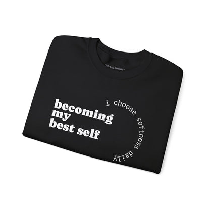 Folded black sweatshirt with “becoming my best self” circular softness quote design.