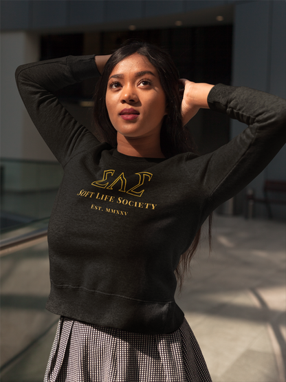 Woman wearing a black sweatshirt with gold Soft Life Society text in an indoor setting