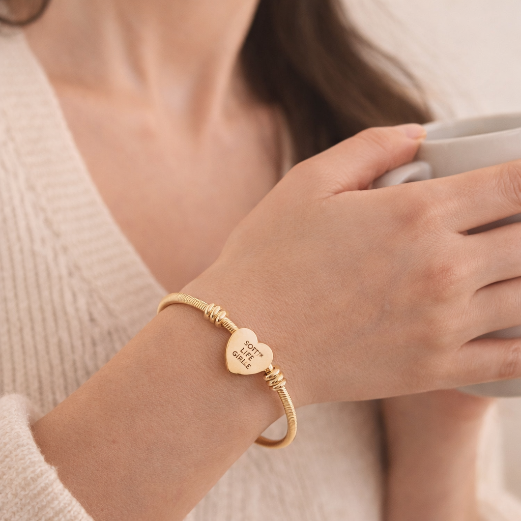 Gold bracelet with a heart-shaped charm worn by a person holding a mug.