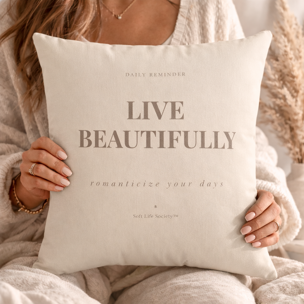 Person holding a pillow with 'Live Beautifully' text in a cozy setting