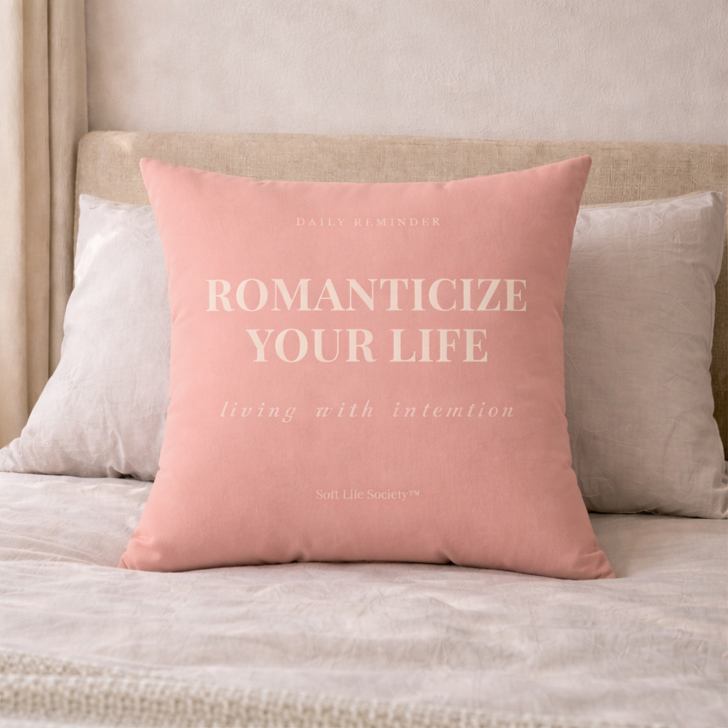Pink pillow with text 'ROMANTICIZE YOUR LIFE' on a beige bed