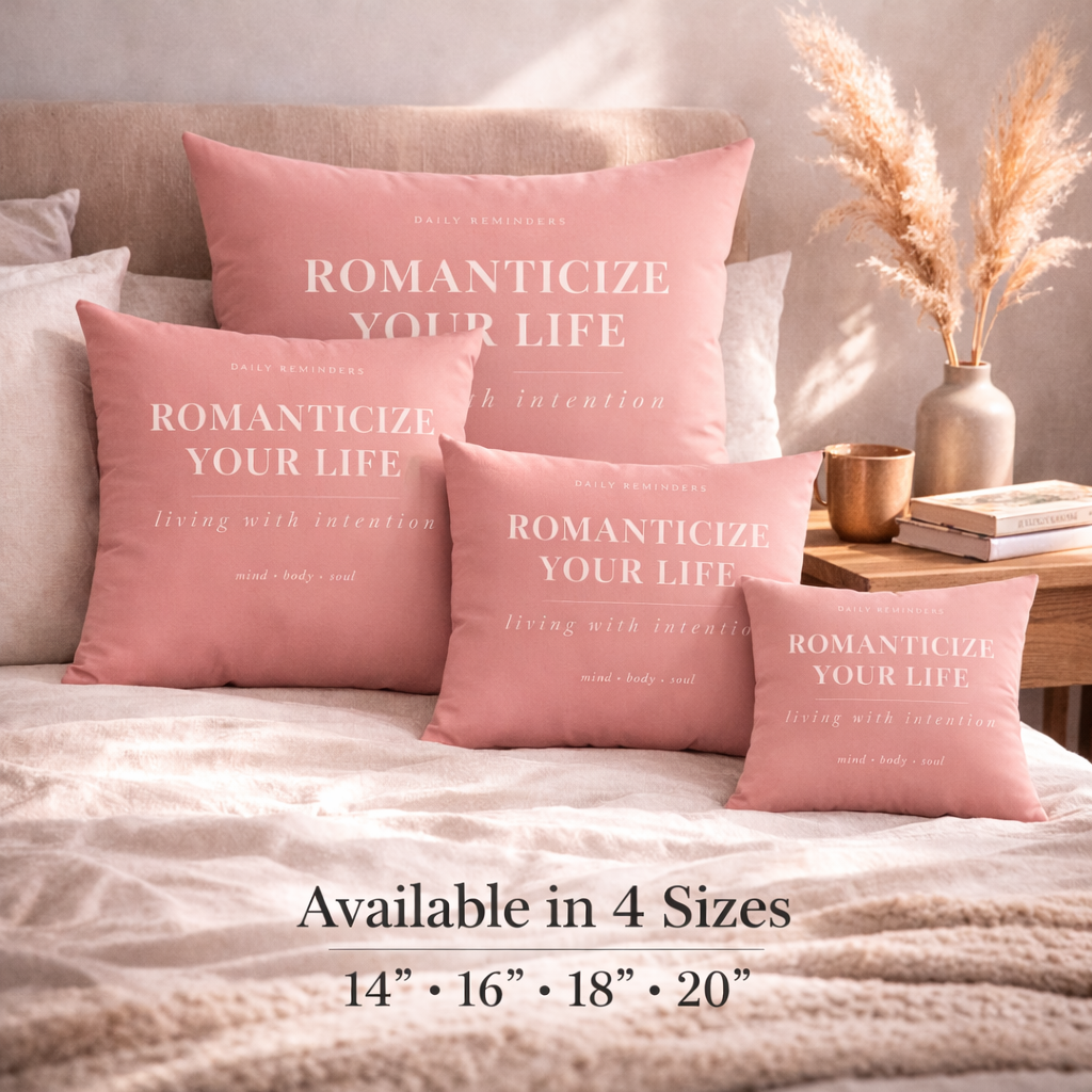 Pink pillows with text on a bed, with a side table and decor items in the background.
