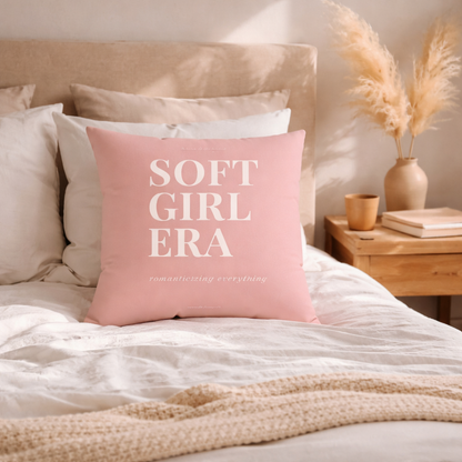 Pink pillow with 'SOFT GIRL ERA' text on a bed with neutral tones.