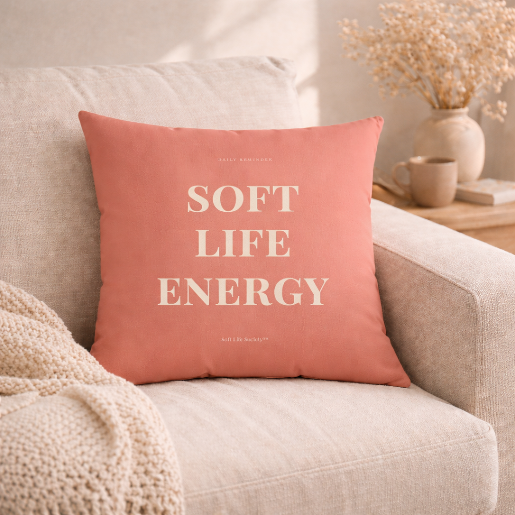 Coral pillow with 'Soft Life Energy' text on a beige couch