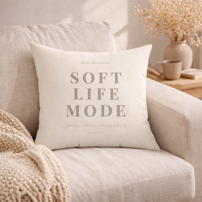 Decorative pillow with 'Soft Life Mode' text on a beige couch.