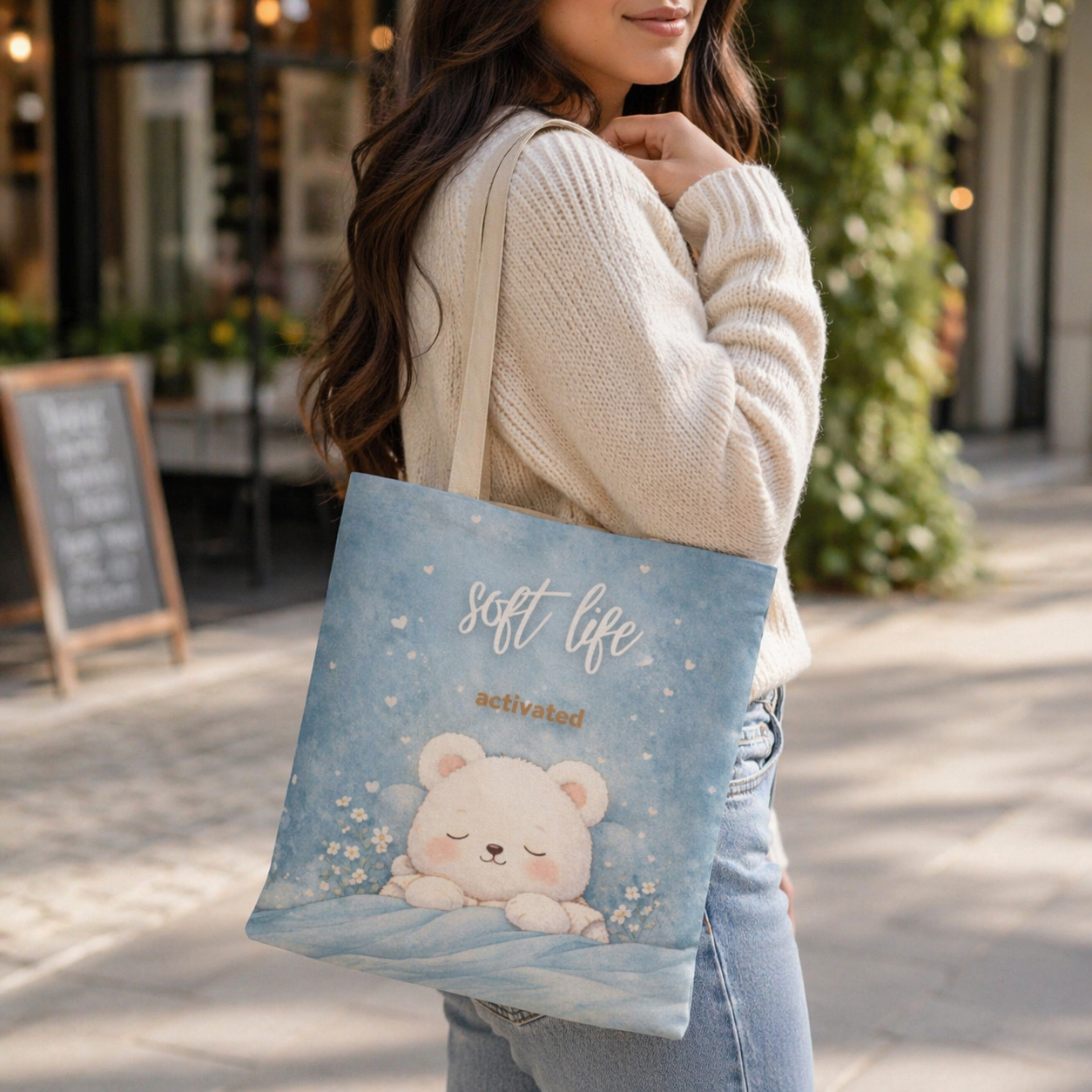 Woman holding a tote bag with a bear design and 'soft life activated' text on a city street.