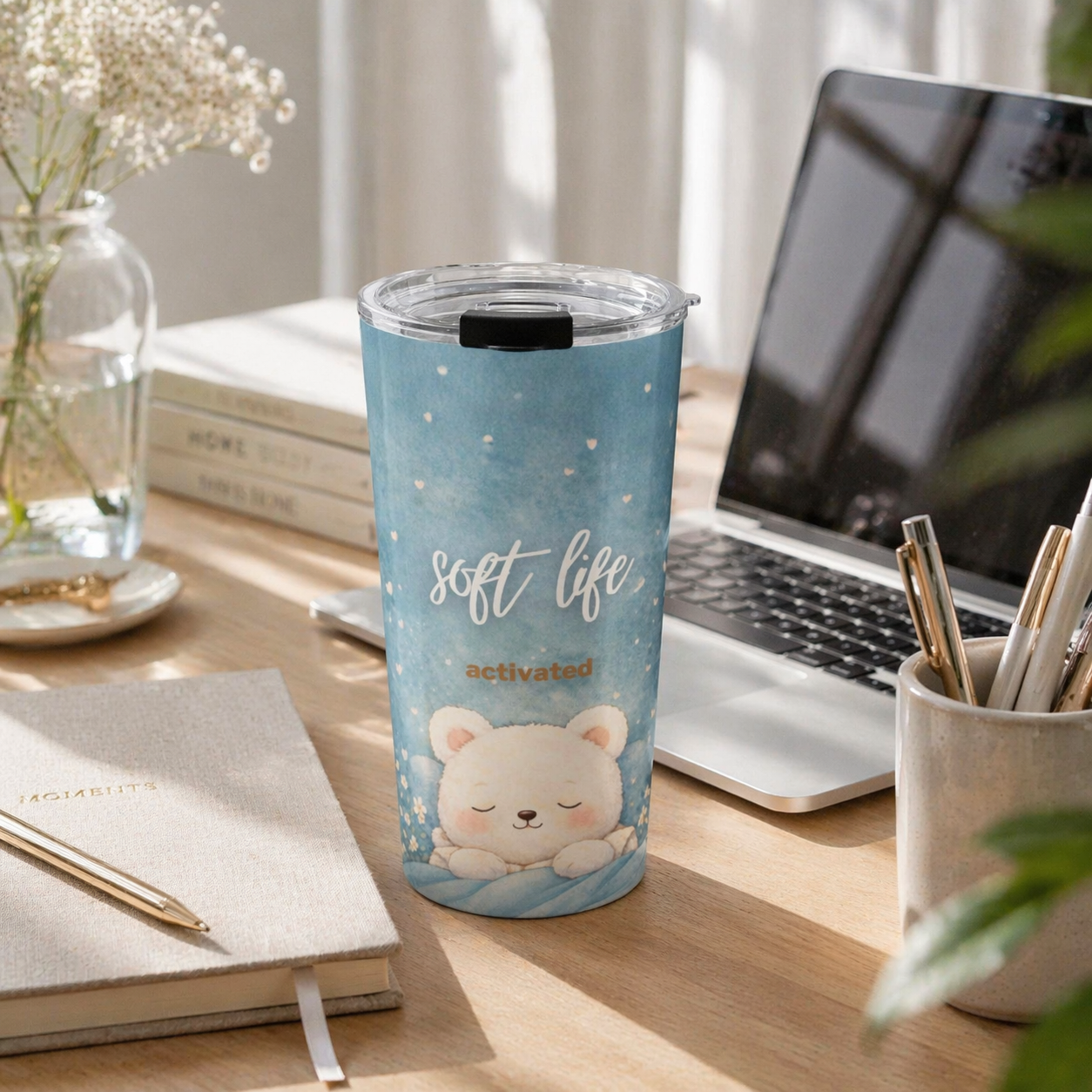 Tumbler with a cute bear design and 'soft life activated' text on a desk with a laptop and books.