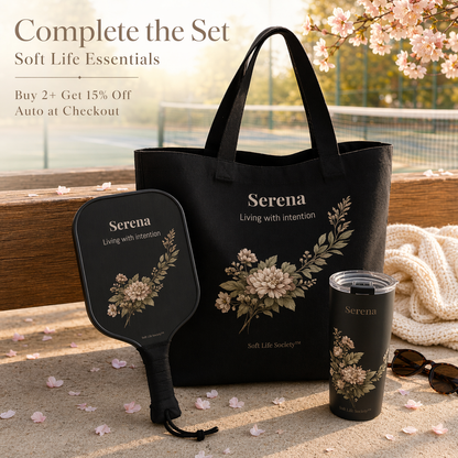 Black tote bag, paddle, and tumbler with floral design and 'Serena' branding on a wooden surface with cherry blossoms.