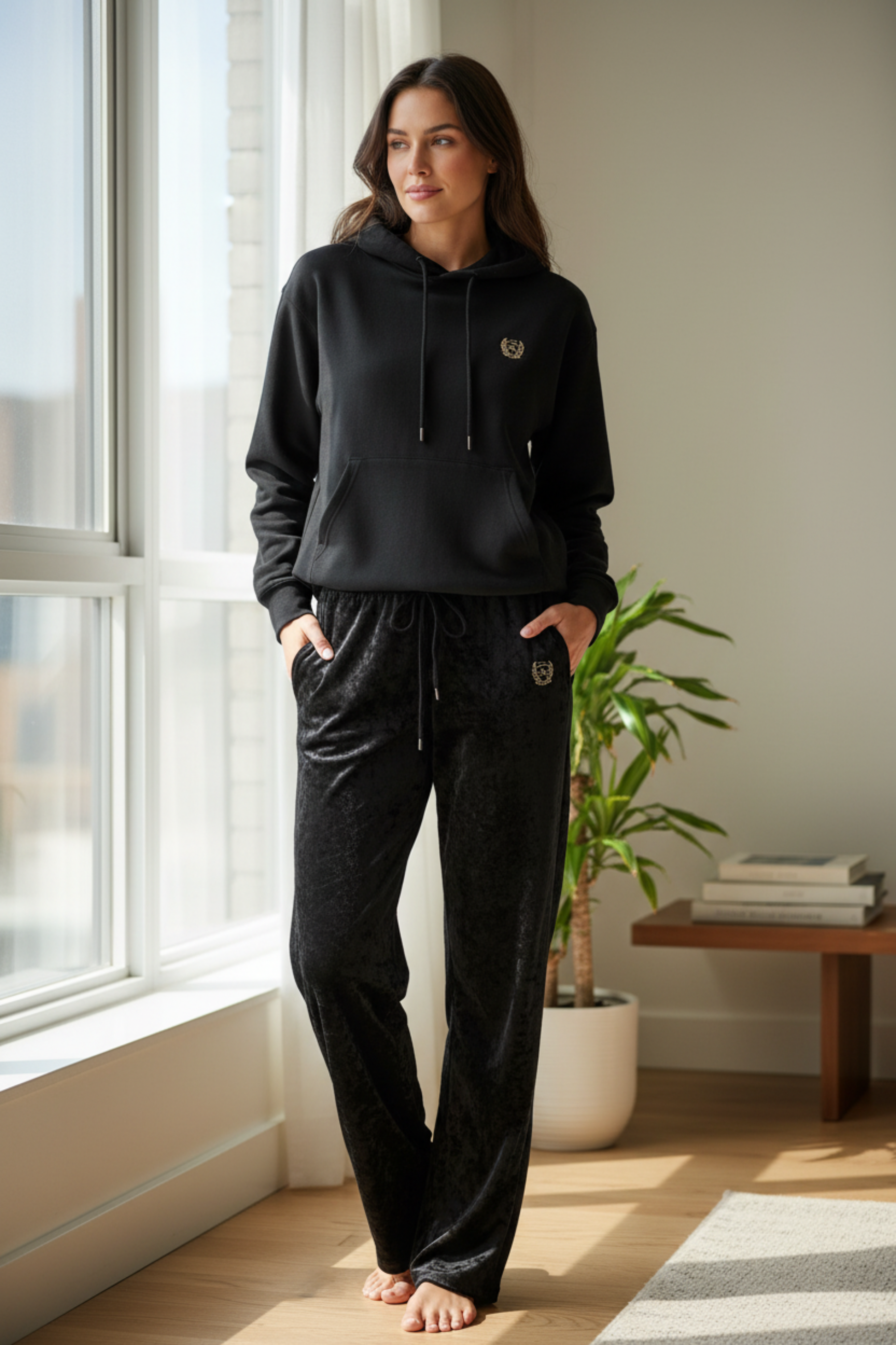 Soft Life Society™ lounge set styled indoors, featuring black crushed velour trousers and hoodie with matching embroidered ΣΛΣ crests for a refined, intentional look.