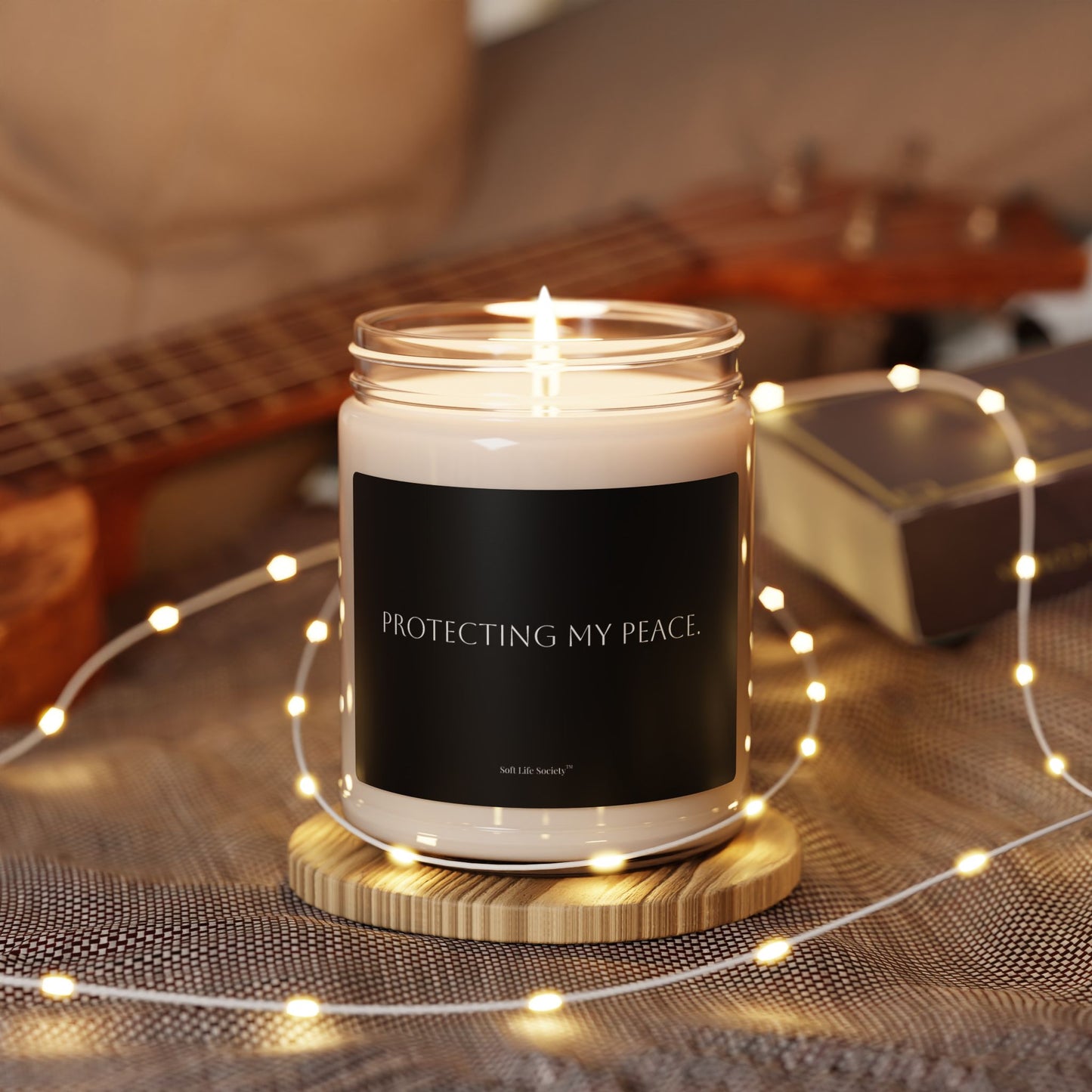 Lit black self-care candle with quote surrounded by warm fairy lights in a cozy living room setting