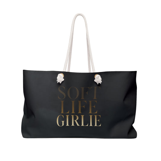 Black Soft Life Girlie weekender tote bag with gold-gradient text and white rope handles, displayed against a white background.