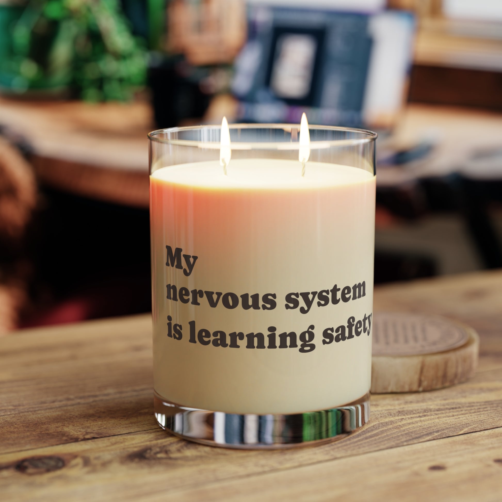 Soft Life Society Candle with text 'My nervous system is learning safety' on a wooden surface.