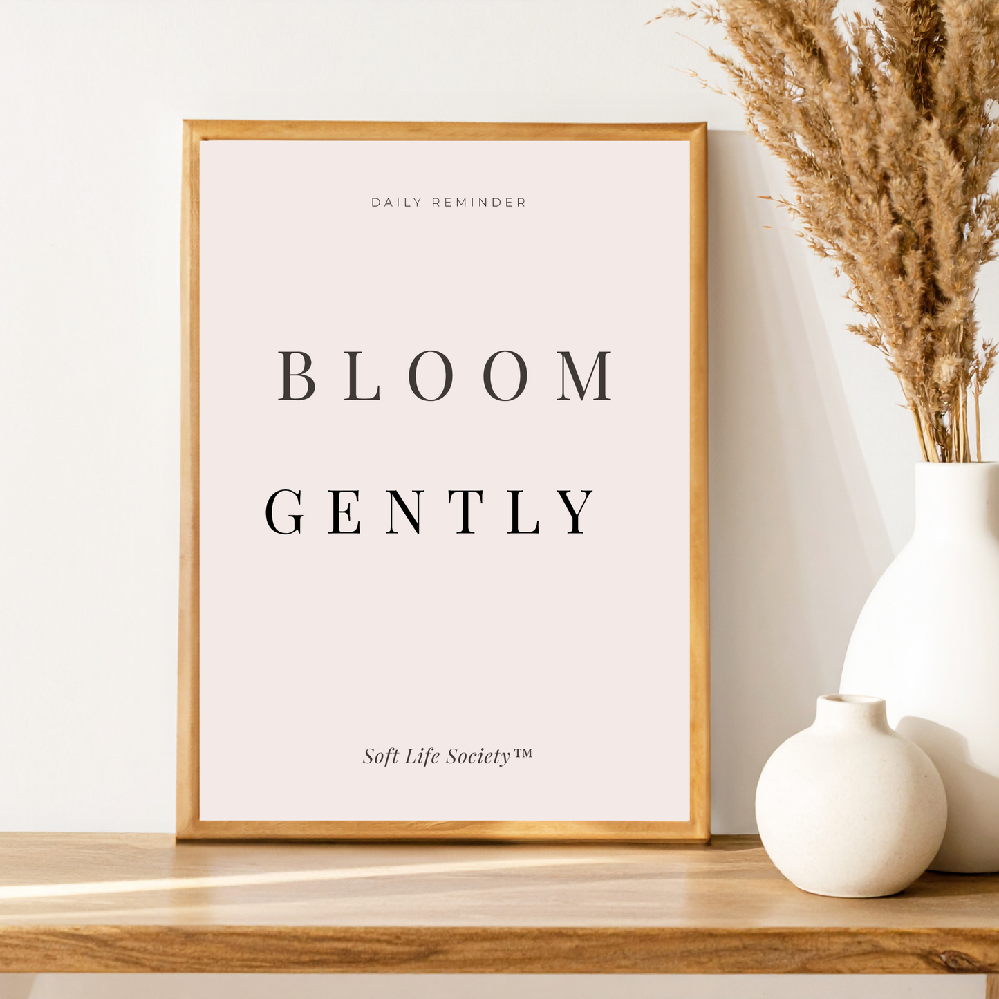 Framed print with 'Bloom Gently' text on a wooden surface with decorative vases.