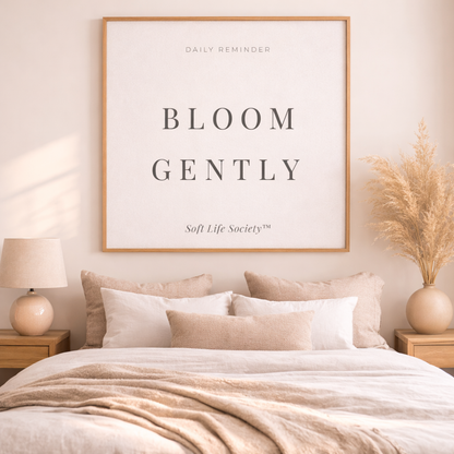 Neatly made bed with pillows and a framed art by Soft Life Society with quote "Bloom Gently" above, in a bedroom setting