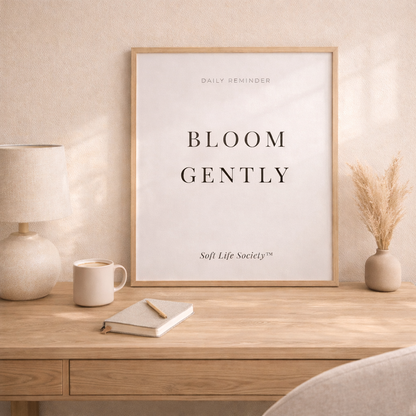 Framed print with 'Bloom Gently' on a wooden desk with a lamp and mug.