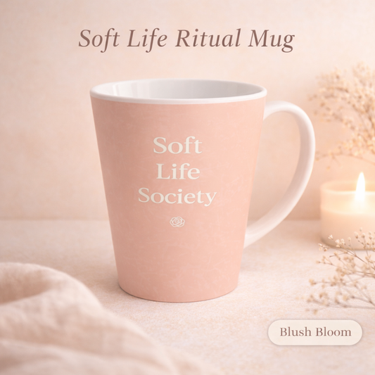 Pink mug with 'Soft Life Society' text on a soft pink background with a candle and flowers.