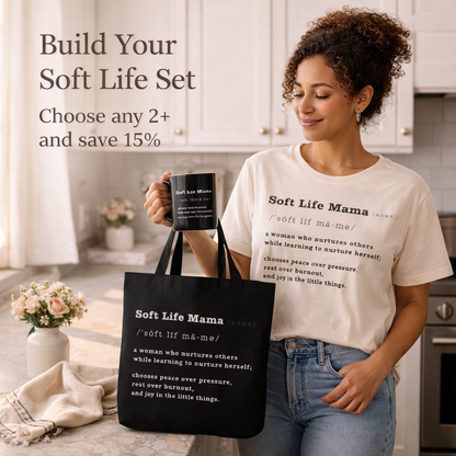 Woman holding a black mug and tote bag with 'Soft Life Mama' text in a kitchen setting.
