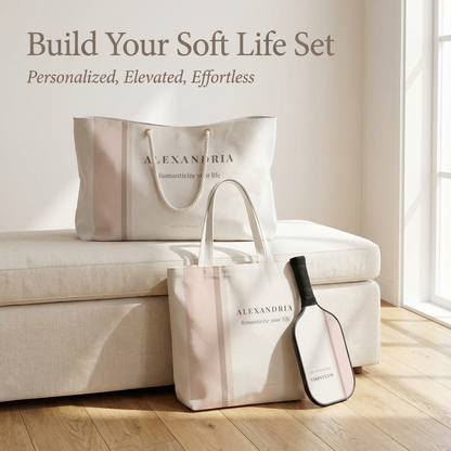 Two tote bags and a pickleball paddle on a couch with 'Alexandria' branding, against a neutral background.