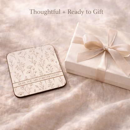 Decorative coaster with floral design and text next to a gift box on a soft surface.