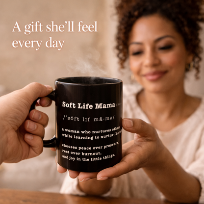 Person gifting a black mug with 'Soft Life Mama' text to woman smiling in the background