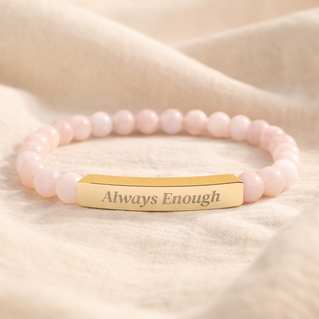 Rose quartz beaded affirmation bracelet with engraved gold bar reading “Always Enough,” photographed on a soft neutral fabric background.