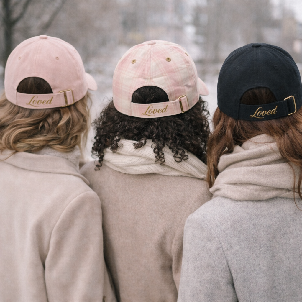 Three people wearing hats with 'Loved' embroidery in a snowy outdoor setting
