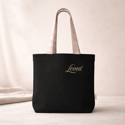 Black tote bag with 'Loved' printed on a light background