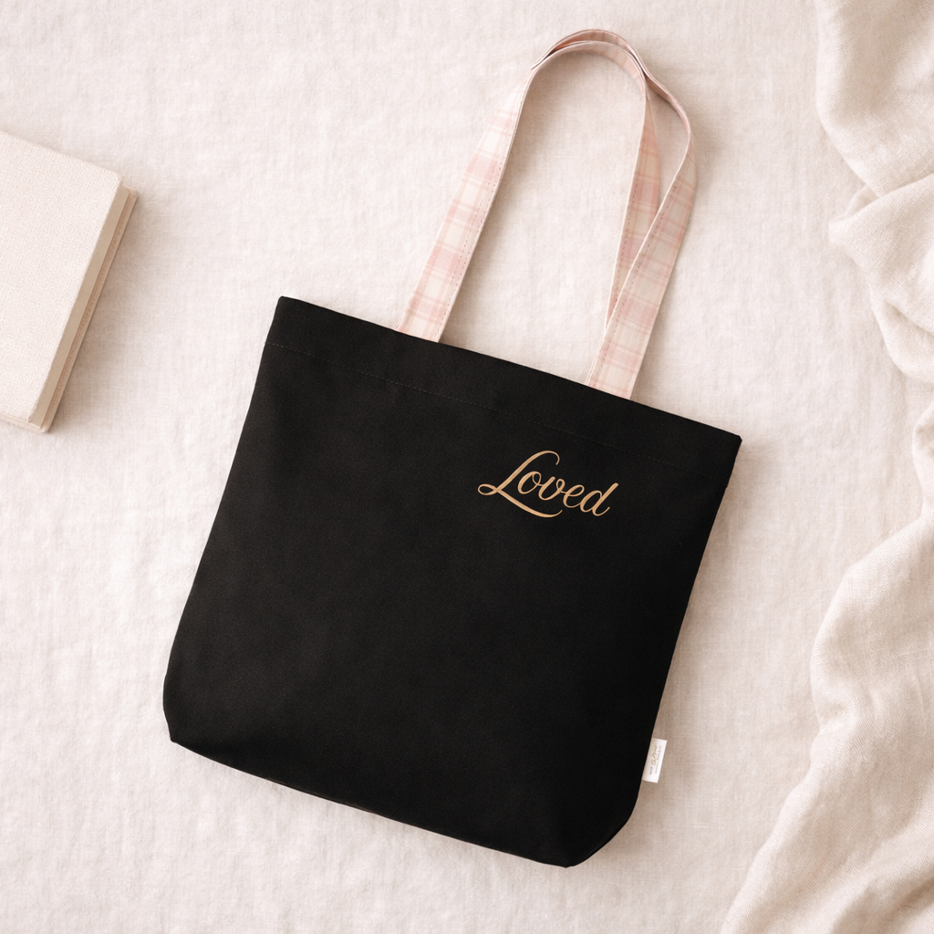 Black tote bag with 'Loved' text in gold on a light background