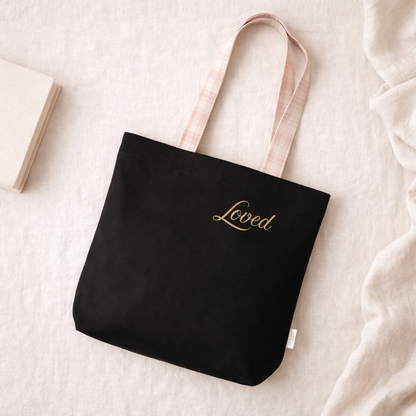 Black tote bag with 'Loved' text in gold on a light background