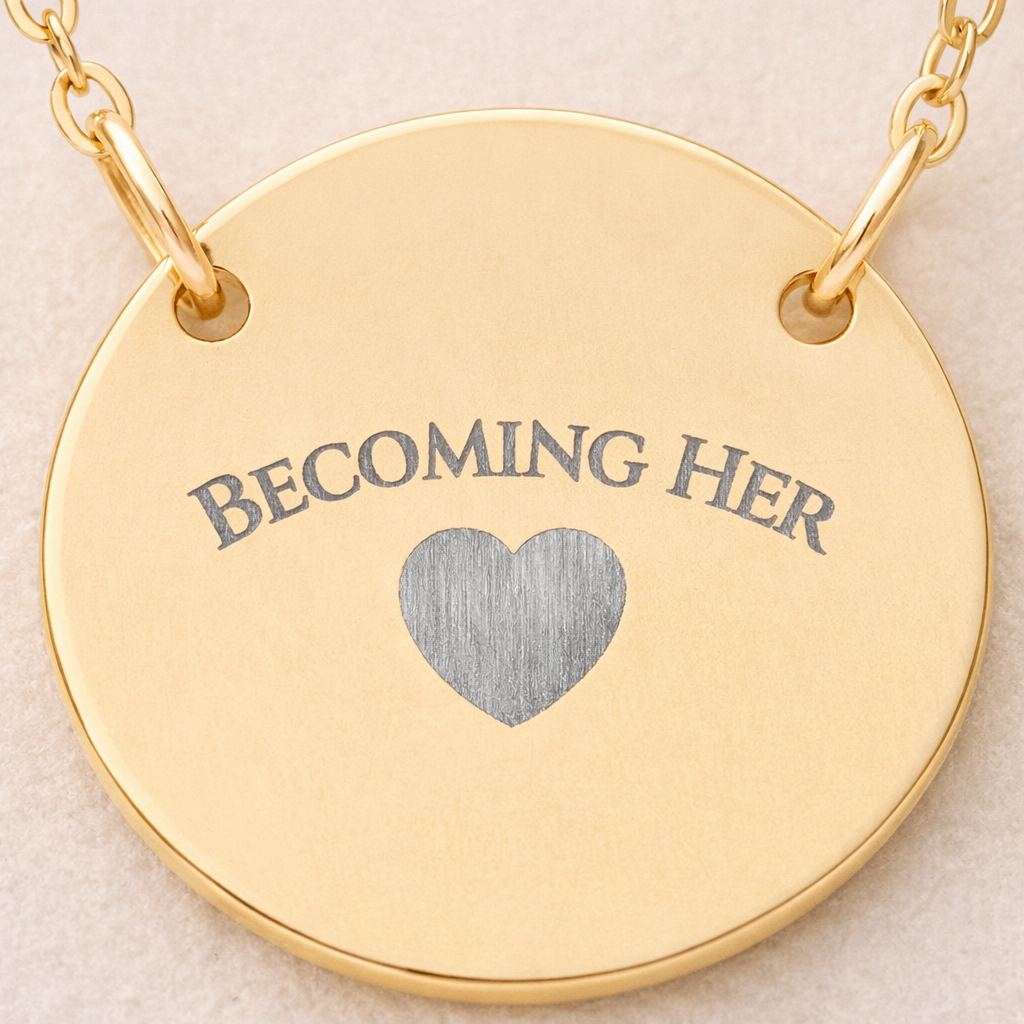 Gold necklace with a round pendant featuring 'BECOMING HER' and a heart symbol on a beige background.