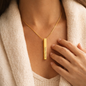 Gold necklace with a bar pendant worn by a person, close-up of the necklace.