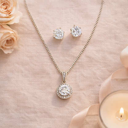 Diamond necklace and earrings on a soft pink fabric background with roses and a candle.