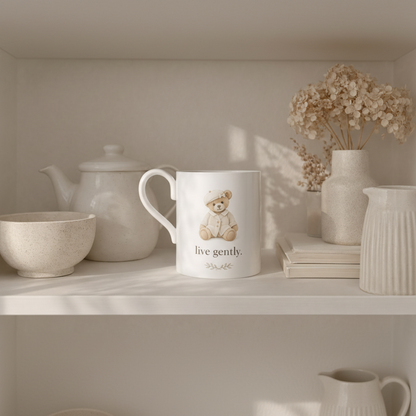 Mug with teddy bear design and 'live gently' text on a shelf with decorative items.