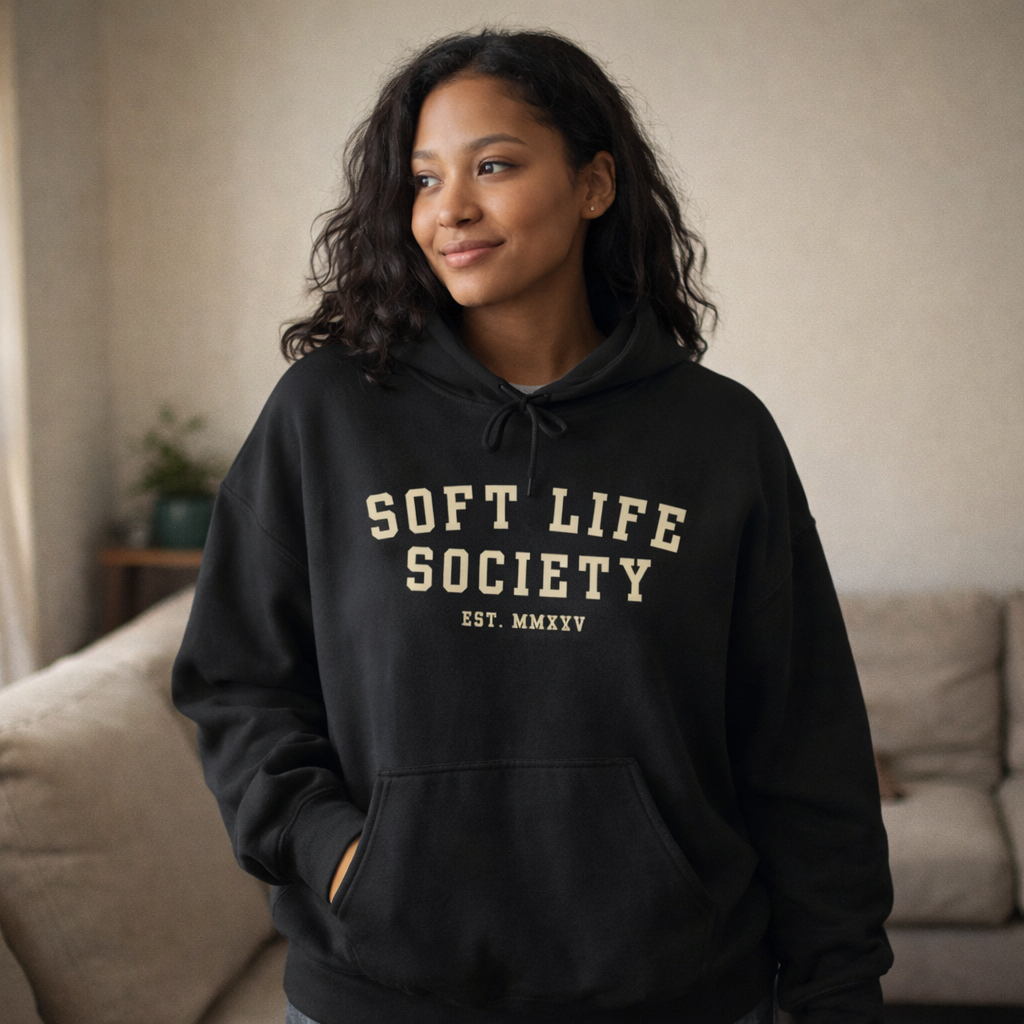 Woman wearing a black hoodie with 'Soft Life Society' text in a living room setting