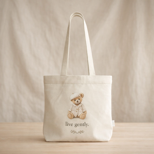 Tote bag with a teddy bear illustration and 'live gently.' text on a neutral background
