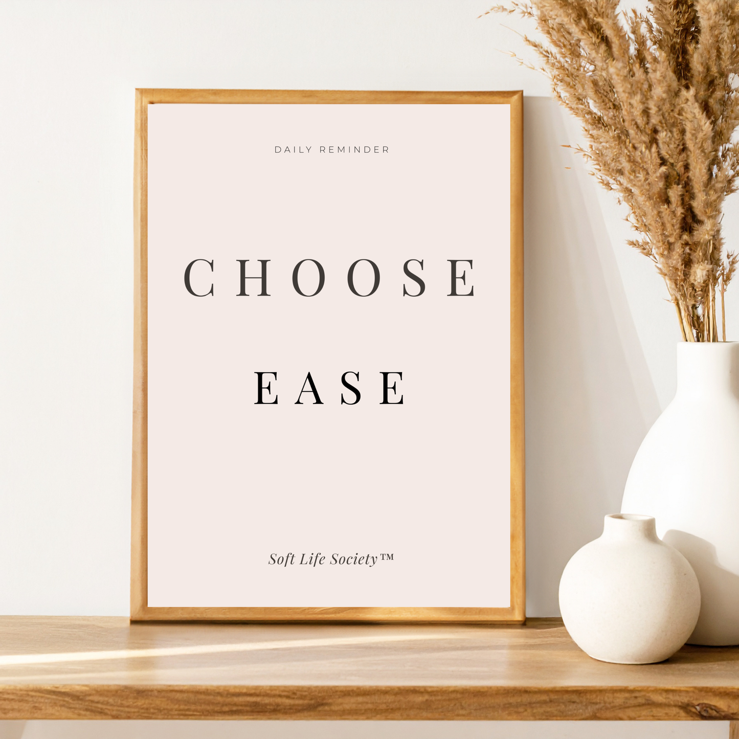 Framed print with 'CHOOSE EASE' text on a wooden shelf with decorative vases.