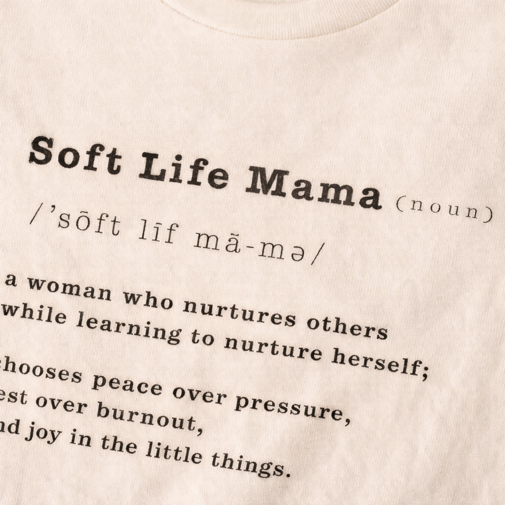 Close up view of beige t-shirt with typography 'Soft Life Mama' definition text on a beige background