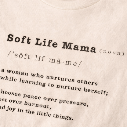 Close up view of beige t-shirt with typography 'Soft Life Mama' definition text on a beige background